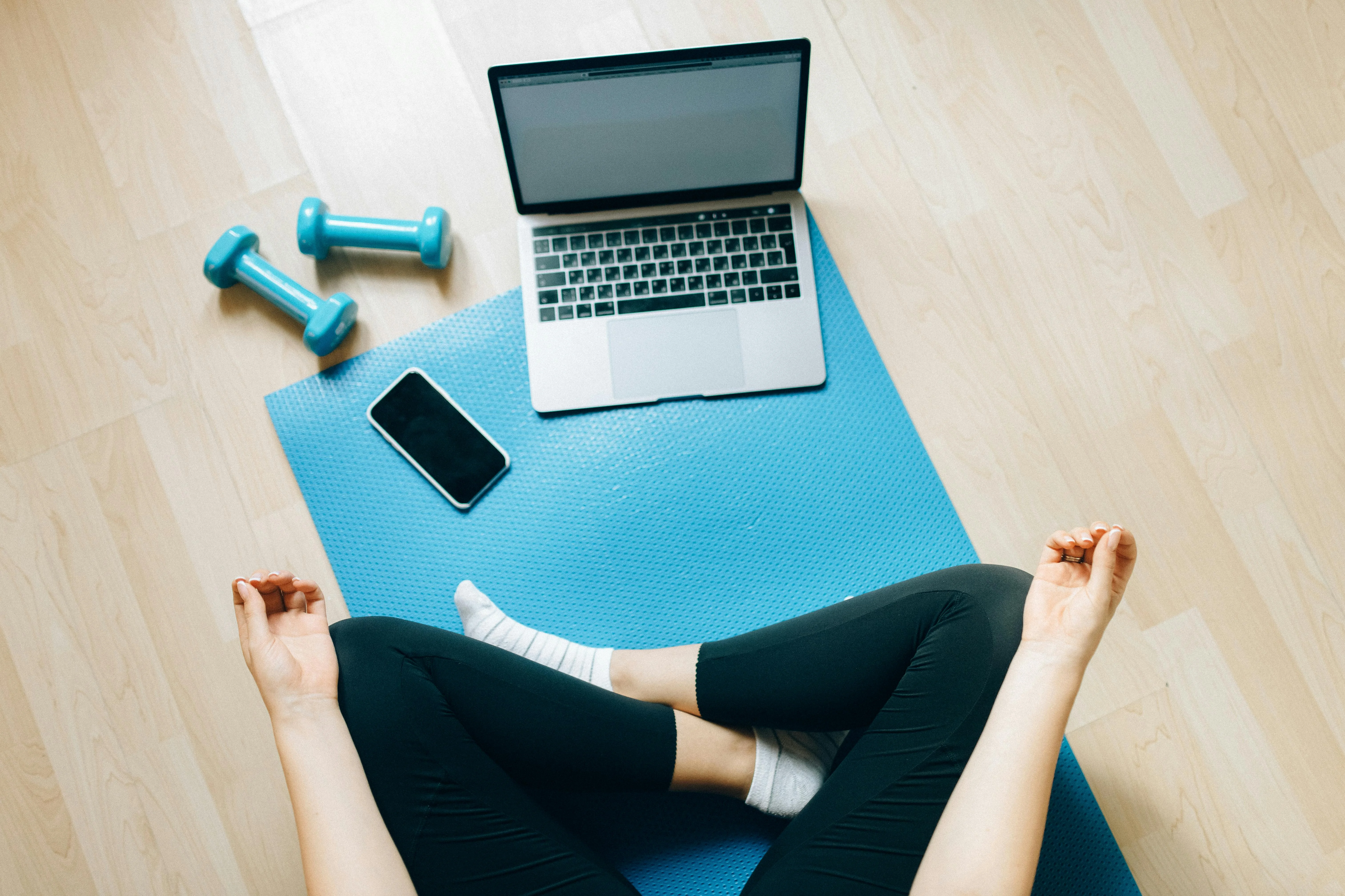 Personne en tailleur sur un tapis bleu avec ordinateur portable et haltères pour un coaching à distance