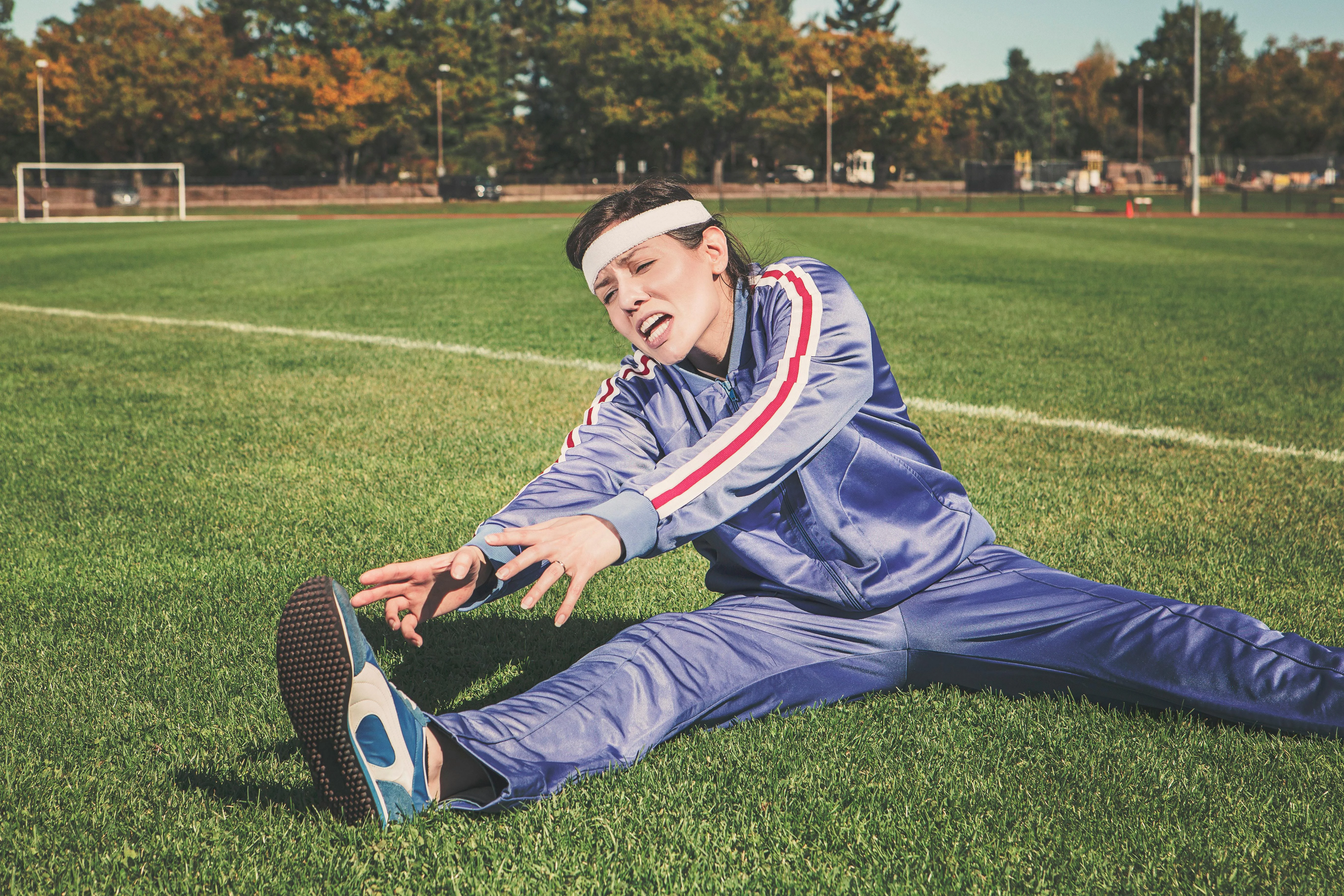 Femme en survêtement bleu en plein étirement sur l'herbe pour reprendre le sport en douceur