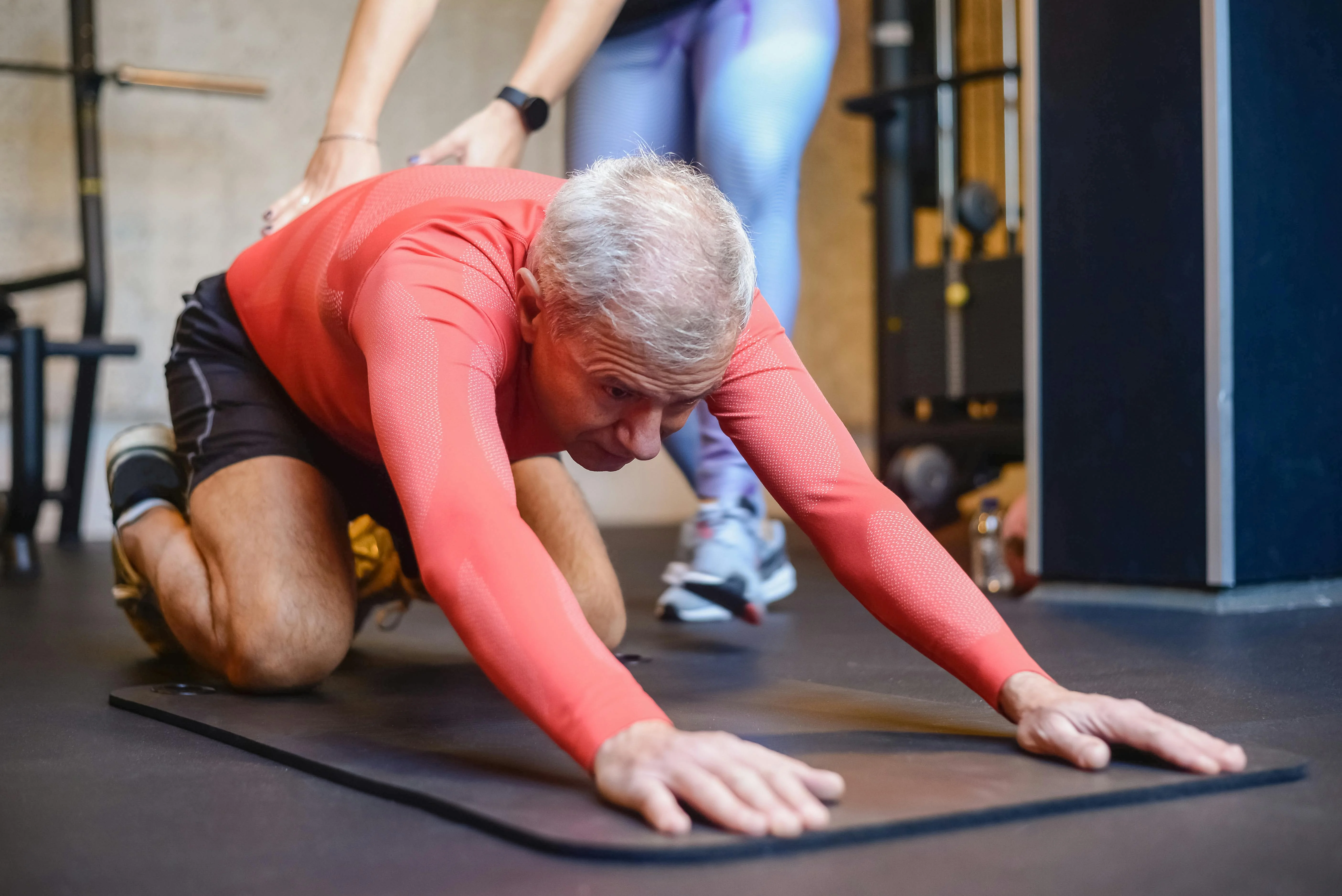 Coach corrigeant la posture d'un senior pendant un étirement au sol en salle de sport